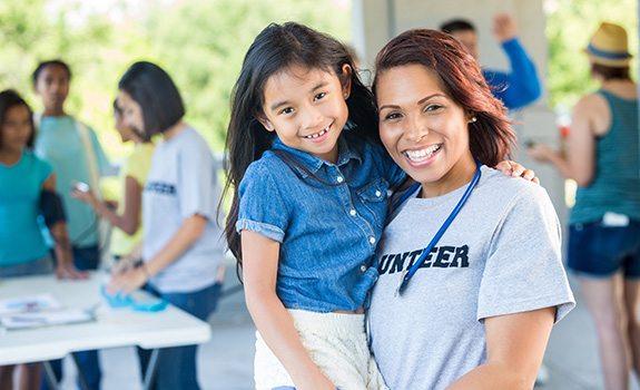 Female volunteer holding a young girl during a volunteer event; both are smiling at the camera